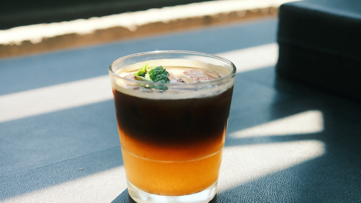 A cold brew gin & tonic in a glass on a sunlit cafe table next to a window