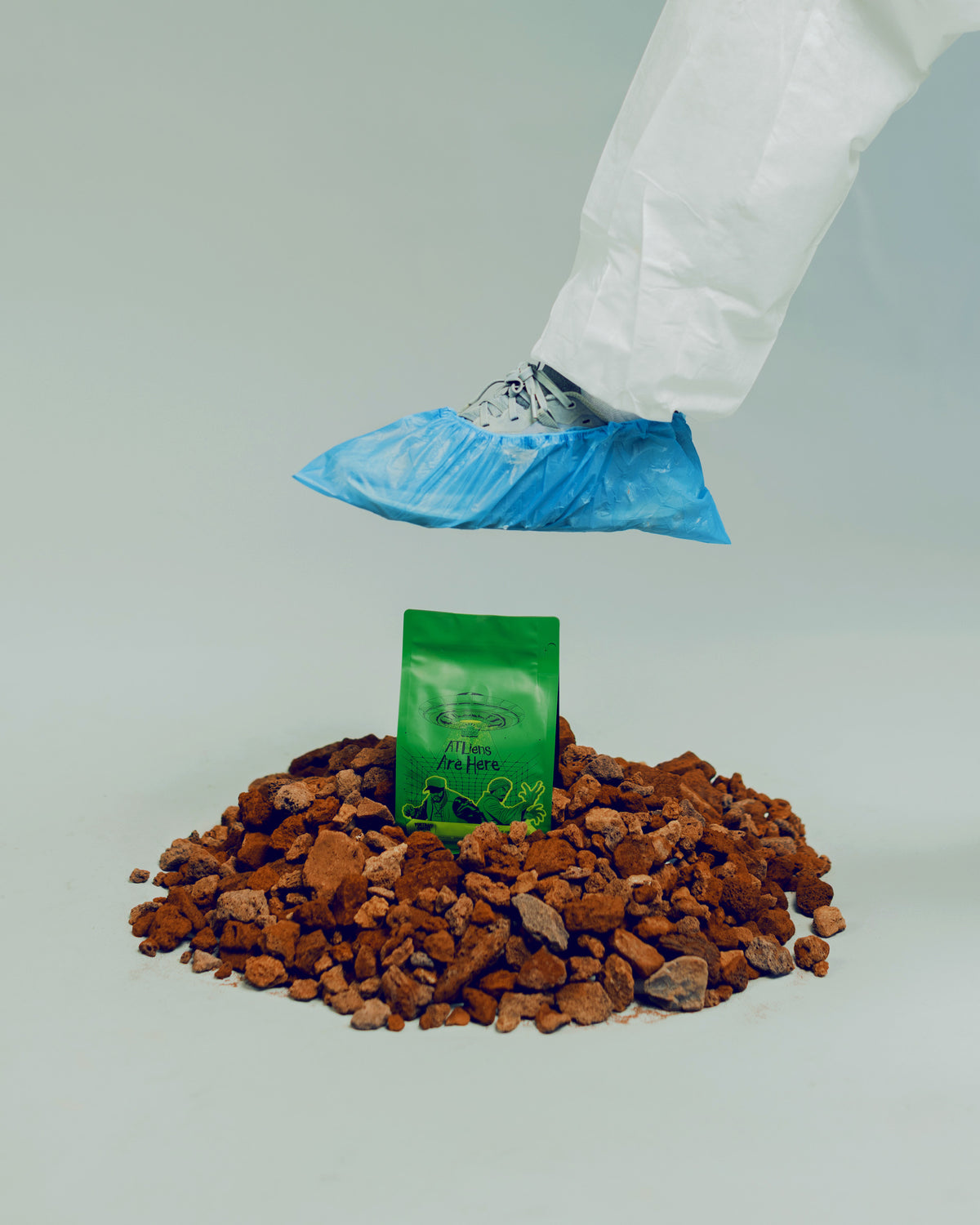 Hazmat-suited figure stepping over the ATLiens coffee bag planted in Georgia red clay