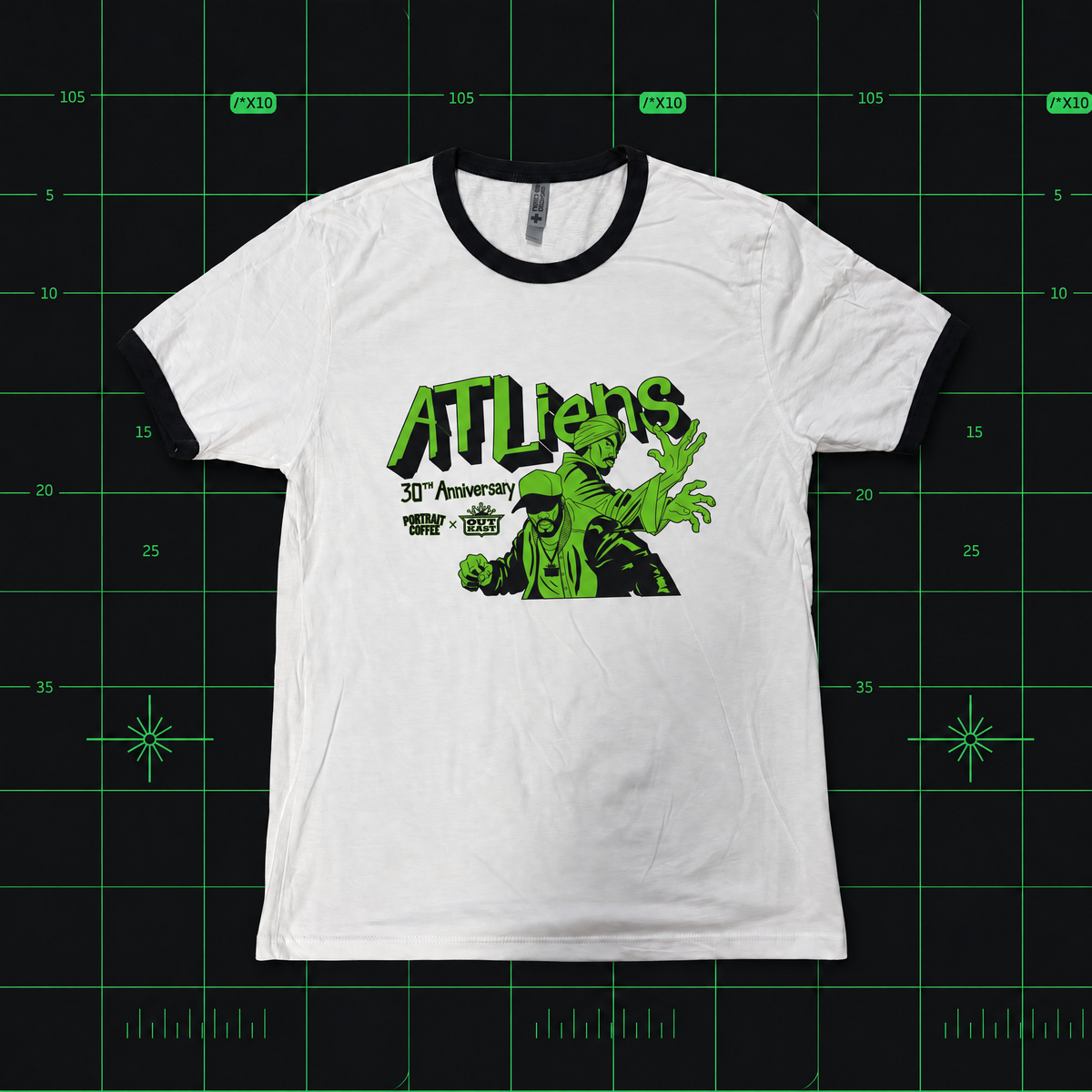 A white ringer t-shirt with black collar and cuffs, featuring a green graphic of a creature and the text 'ATLIENS 30th Anniversary' on the front, displayed flat against a black grid background.