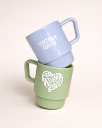 Two mugs, one light blue and one green, stacked on a white background.